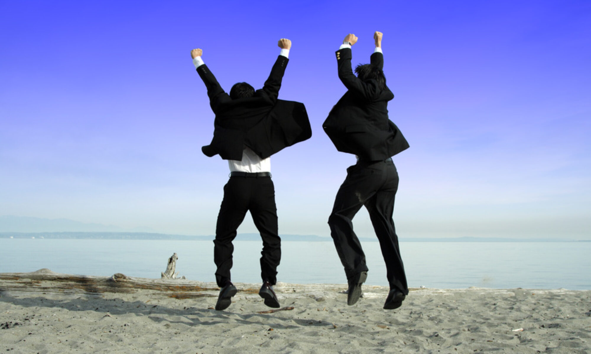 Sommerferien Two businessmen jumping and celebrating on the beach